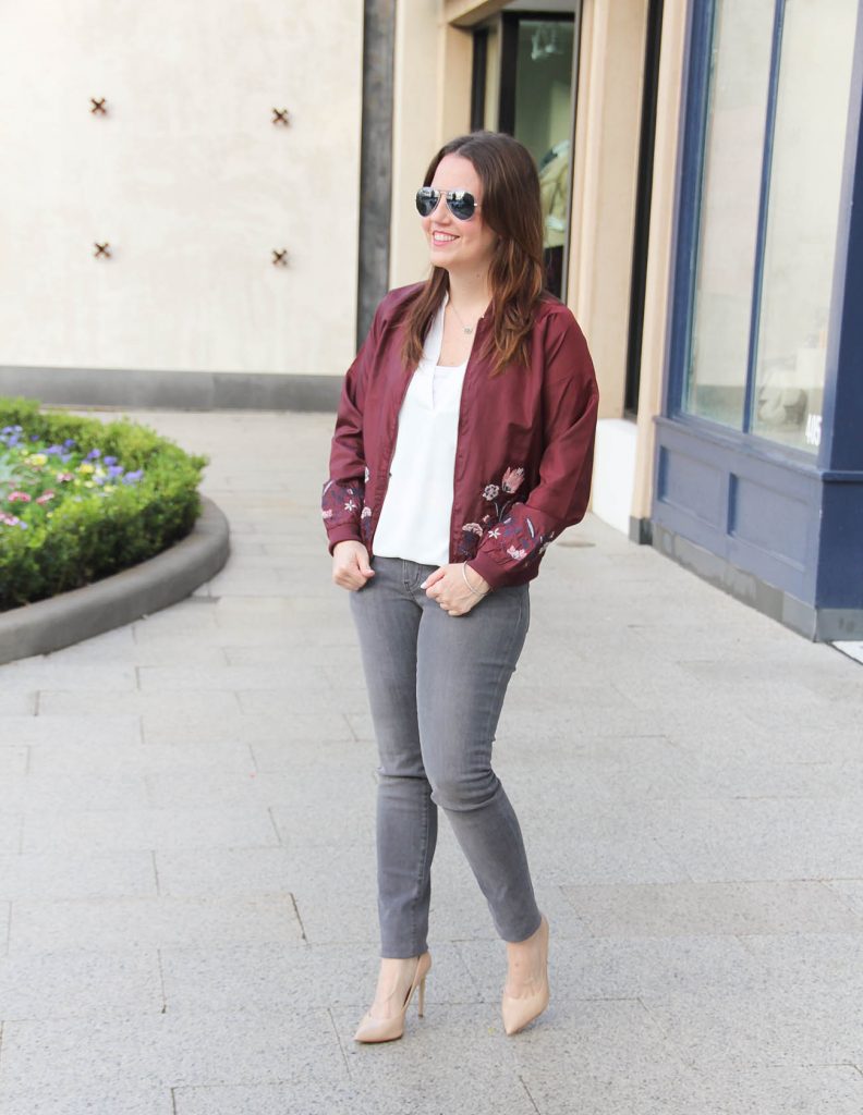 Houston Fashion Blogger styles a winter outfit idea featuring a floral bomber jacket, gray skinny jeans and heels.