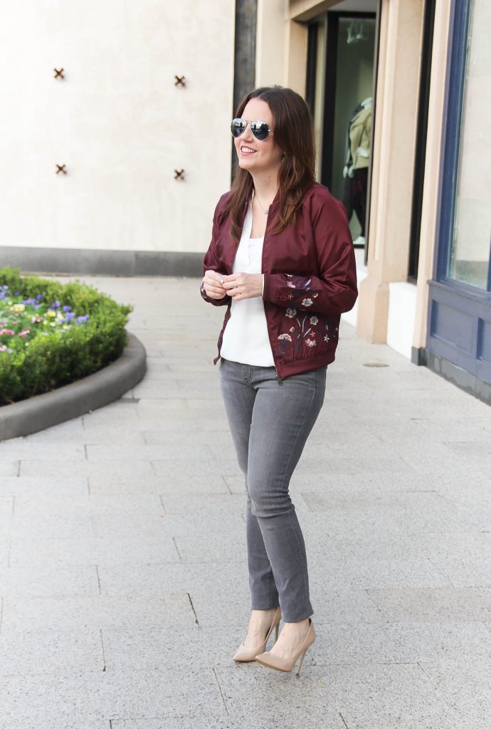 Houston Fashion Blogger Lady in Violet styles a casual weekend outfit featuring a floral bomber jacket and gray jeans with nude heels.