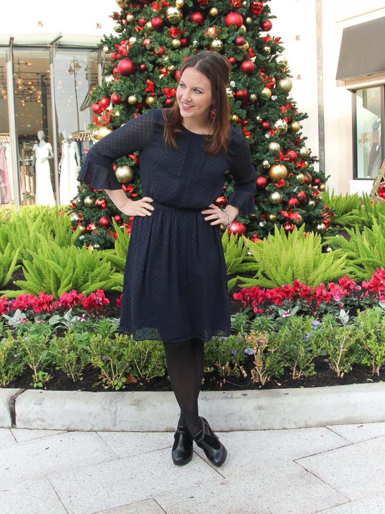 Houston Fashion blogger, Lady in Violet styles a holiday office party outfit including a navy dress with black tights and pink statement earrings.