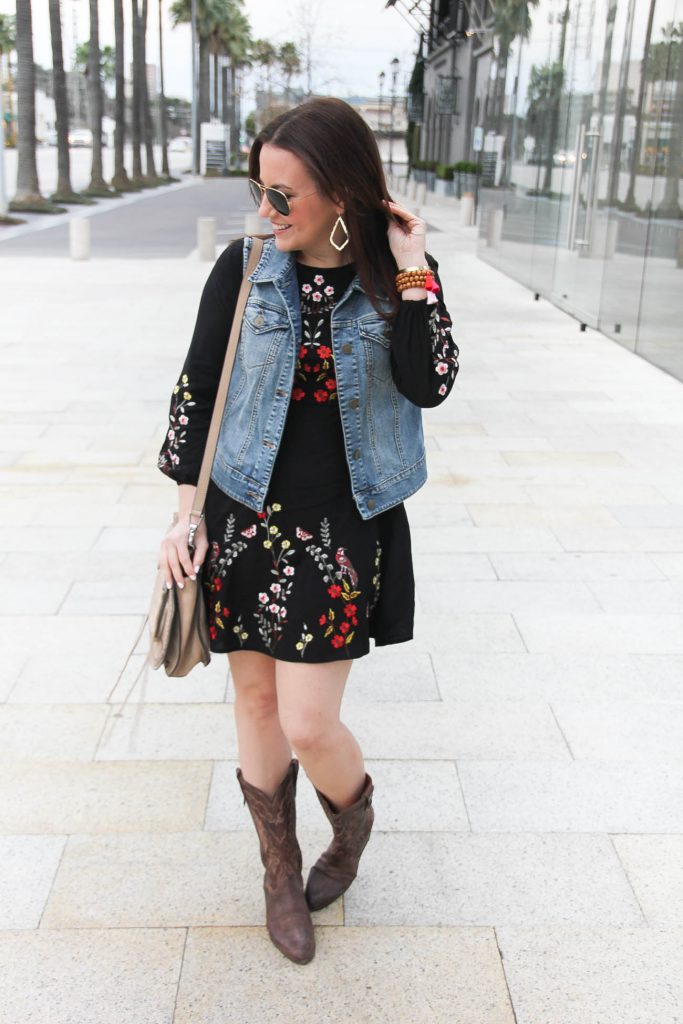 Houston Style Blogger wears a country music festival outfit including a floral embroidered dress with a denim vest and cowboy boots.