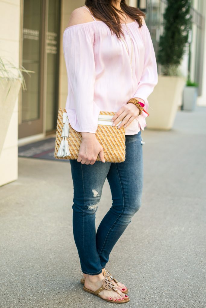 Houston fashion blogger styles a cute casual weekend outfit featuring a pink cold shoulder top with distressed jeans and a straw clutch.