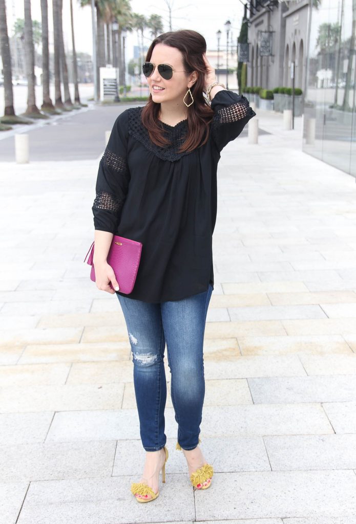 Houston Fashion Blogger wears spring outfit idea including black crochet blouse, distressed jeans, and yellow fringe sandals.