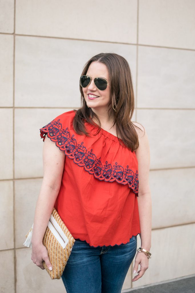 Houston fashion blogger styles a summer party outfit idea including a red one shoulder top with jeans and a cute clutch.