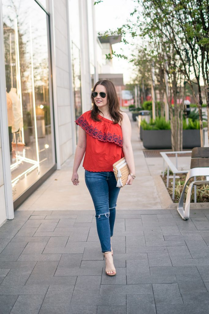 Fashion blogger shows houston street style in a spring outfit idea featuring a red one shoulder top with distressed jeans.