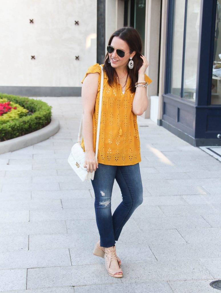 Houston fashion blogger Lady in Violet styles a causal weekend outfit including a yellow top with distressed jeans and nude wedges.